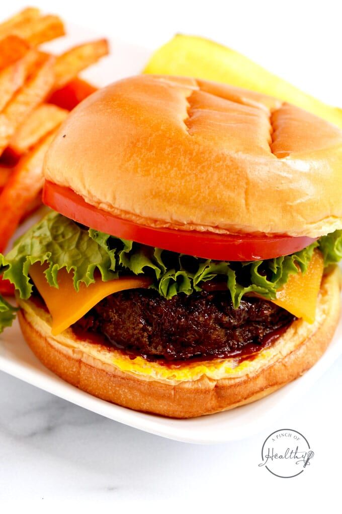 Closeup of hand salting beef burgers cooking on electric grill at