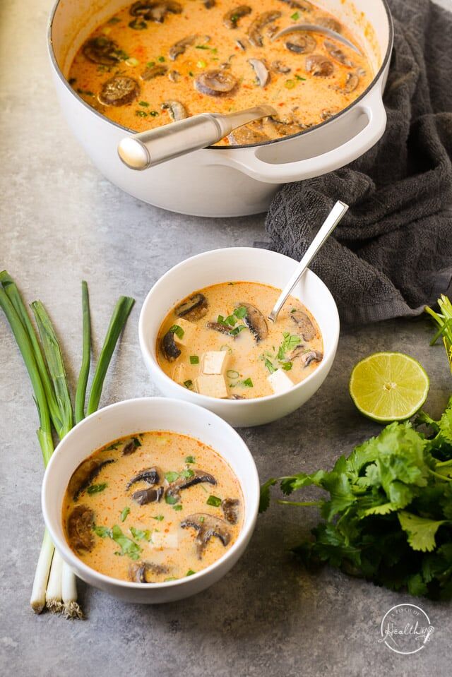 Thai coconut soup in two white bowls on gray surface with lime, green onion and cilantro